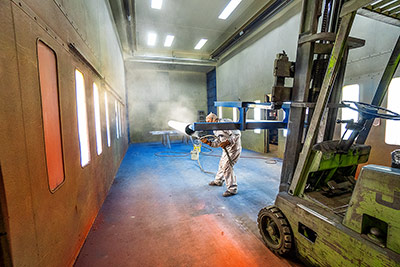Worker paints a pipe in a large paint booth